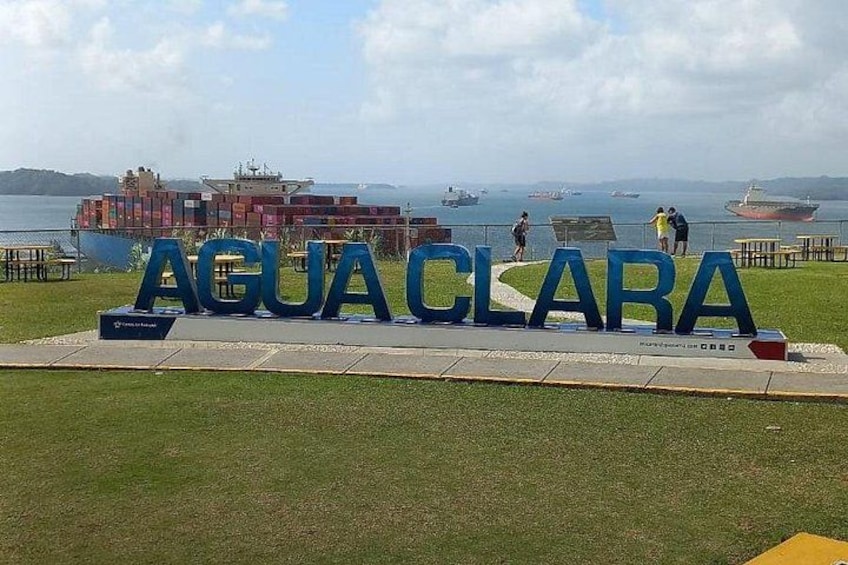 Un letrero con 'AGUACLARA' en letras grandes, un área verde, una masa de agua y un carguero al fondo. 3