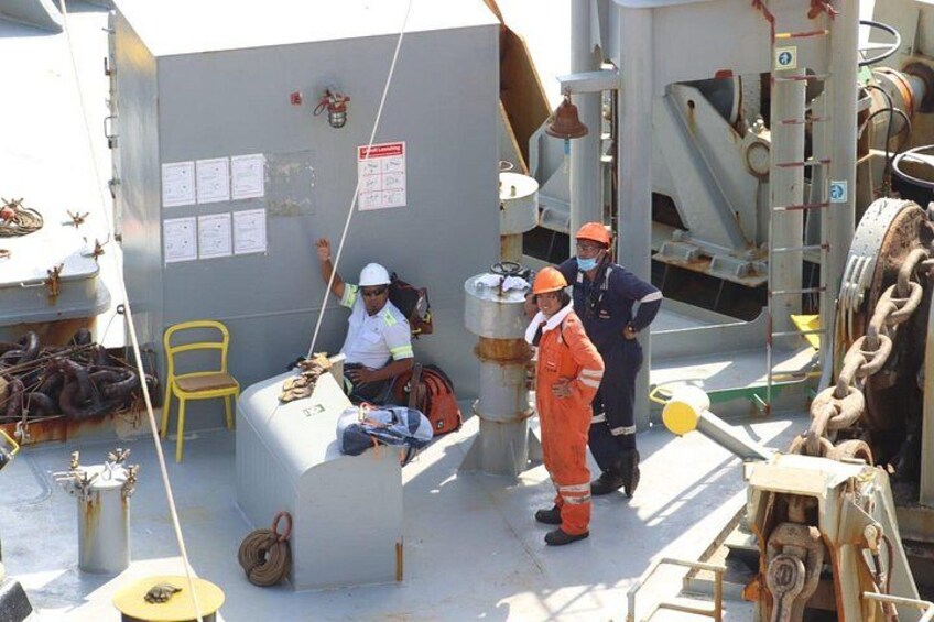 Workers in orange safety gear on a ship deck, a yellow chair, and industrial equipment. 4