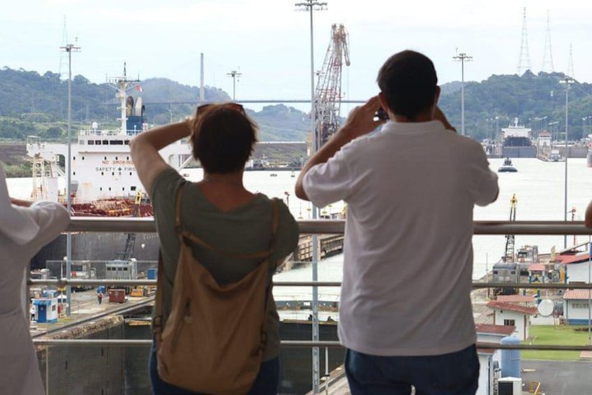 Two people standing by a railing, overlooking a harbor with ships and industrial structures. 2