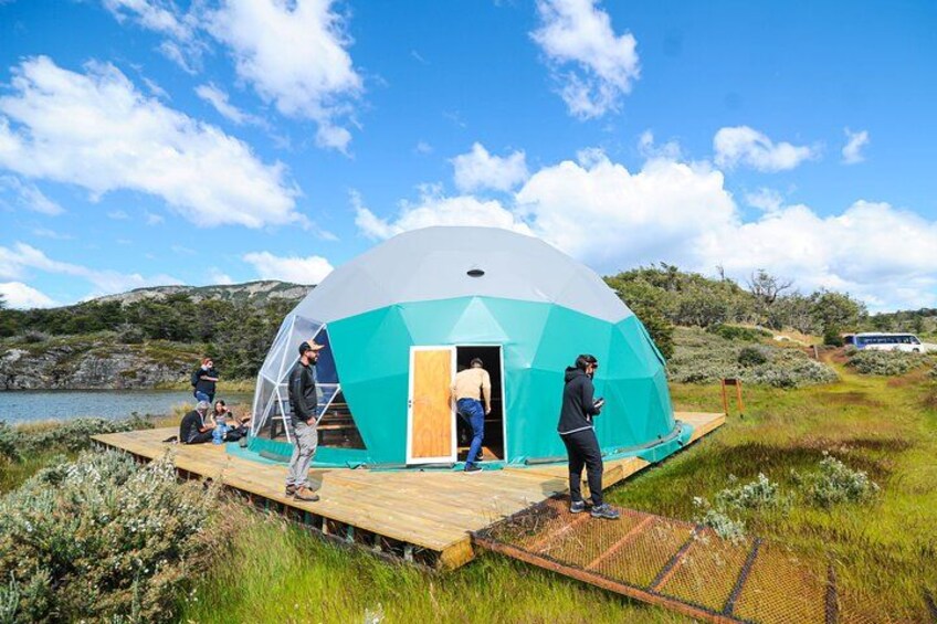 A geodesic dome structure with a wooden platform, surrounded by grass and hills. 4