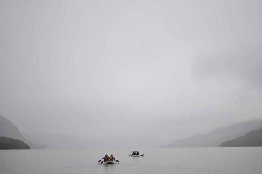 Un lago tranquilo con dos barcos y colinas brumosas al fondo. 4