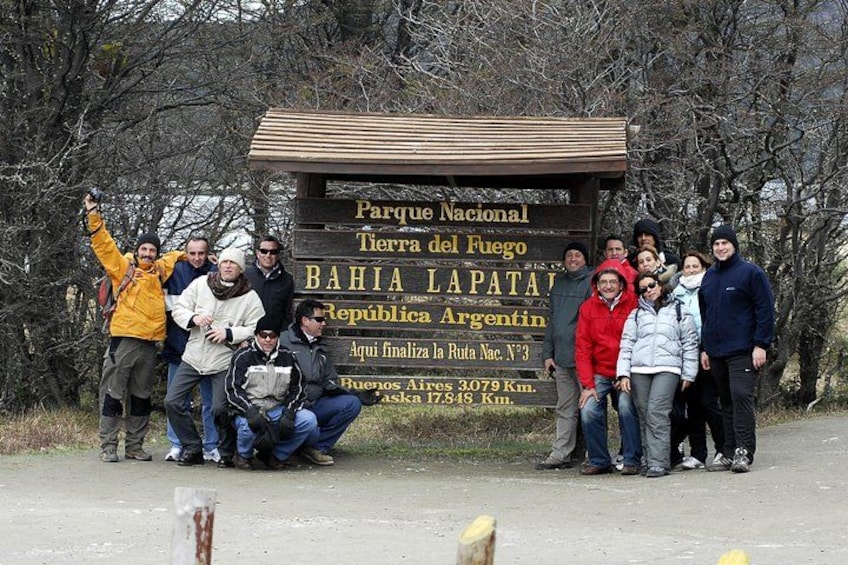 Un grupo de personas posando frente a un cartel con información sobre un parque nacional y distancias a Buenos Aires y Aska. 2