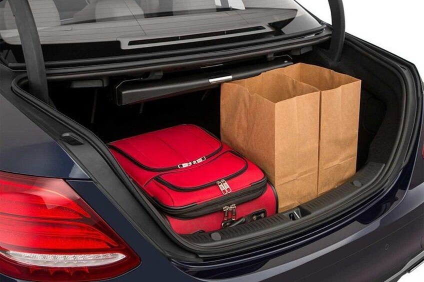 Ein Auto mit geöffnetem Kofferraum, darin ein roter Koffer und eine braune Papiertüte. 2
