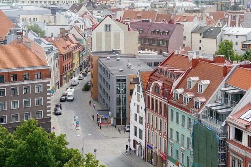 Eine Straße gesäumt von historischen Gebäuden, einem modernen Glasbau und einer begrünten Baustelle. 4