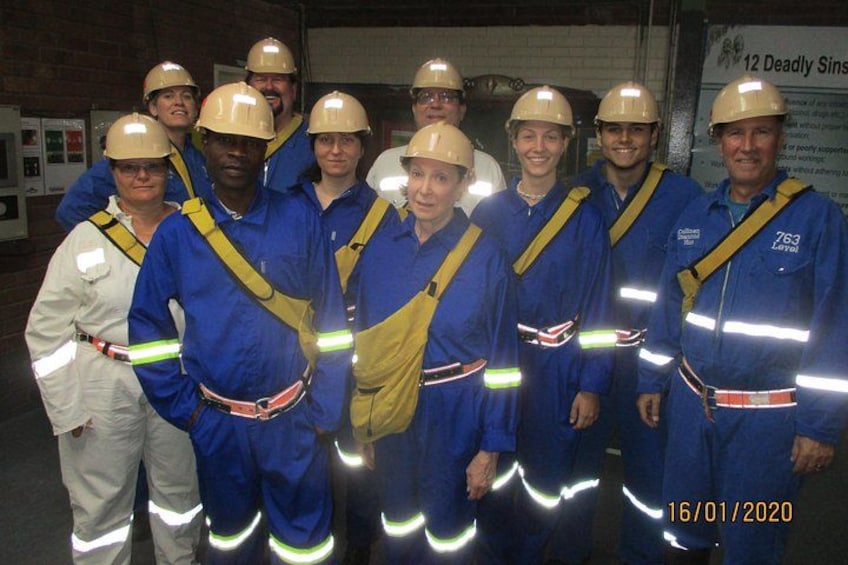 A group of people in blue and white safety gear, including helmets and reflective stripes, standing indoors. 3