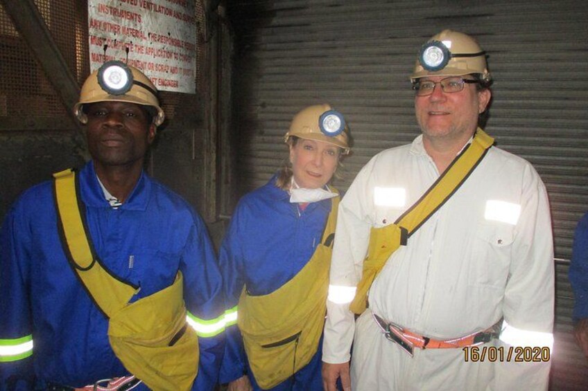 Three people in safety gear, including hard hats and reflective vests, standing in a dimly lit industrial setting. 2