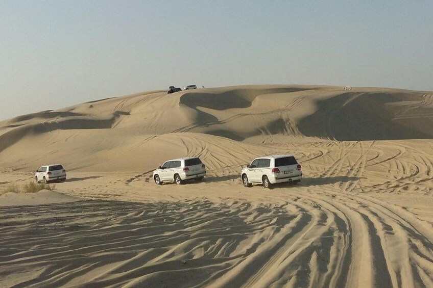 Paisaje desértico con dunas de arena y cuatro SUVs blancos estacionados sobre la arena. 2