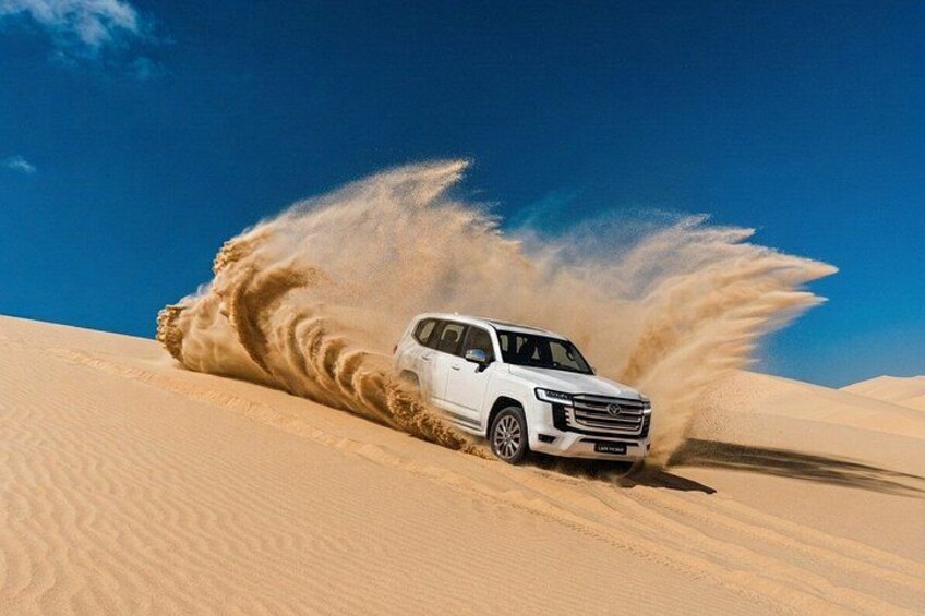 Un SUV blanco circulando por un desierto, levantando arena a su alrededor. 1