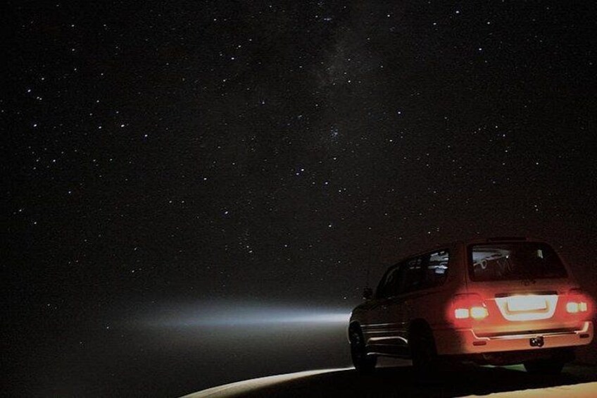 A car driving at night with a starry sky and a faint light in the distance. 2