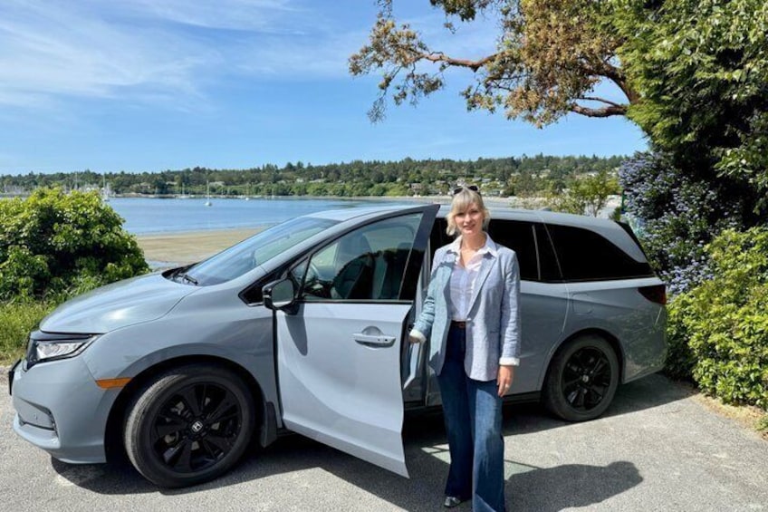 A silver minivan parked by a lake with greenery and a clear sky in the background. 2
