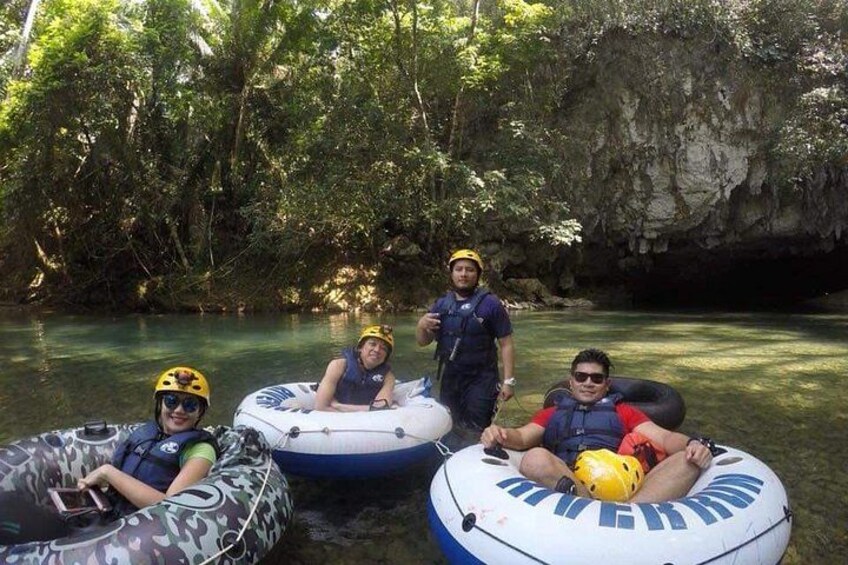 People in inflatable rafts on a river surrounded by greenery and a rocky cliff. 4