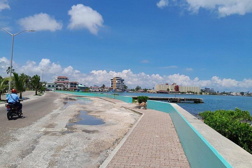 Una carretera costera con un motociclista, una masa de agua y edificios al fondo. 5