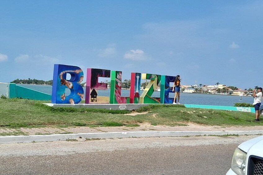 Un letrero colorido con la palabra 'Belize' y una playa al fondo. 5