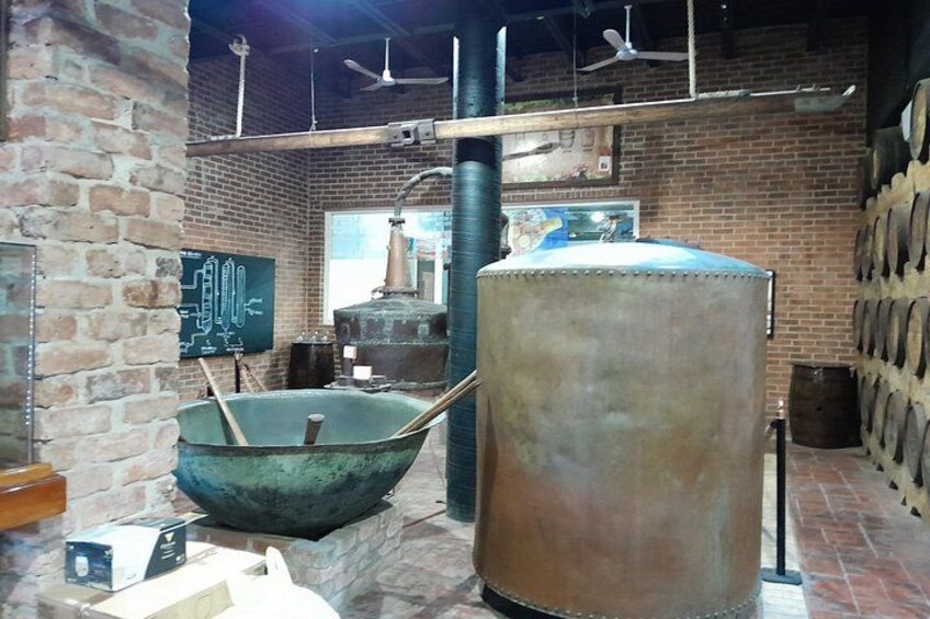 Een gebouw van baksteen met grote metalen vaten, een schoolbord met tekeningen en een houten vat. 4