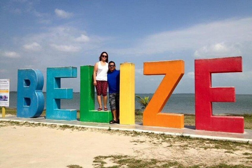 De grandes lettres colorées épellent le mot « BELIZE » sur une plage, avec l’océan en arrière-plan. 2