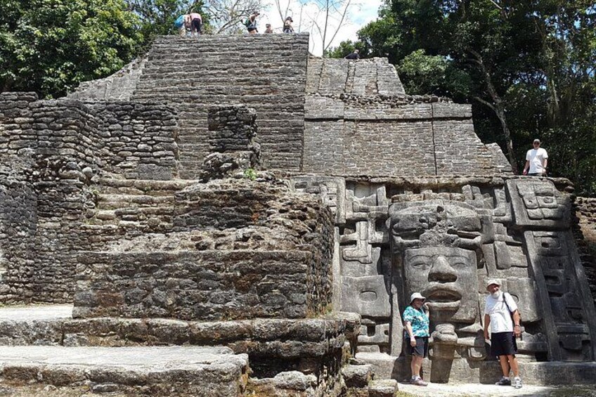 An ancient stone structure with carvings, including a large face, and people standing on the steps. 1