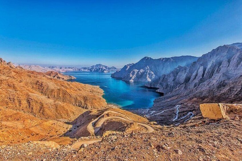 Een bergachtig landschap met een helderblauw meer en een slingerende weg. 1