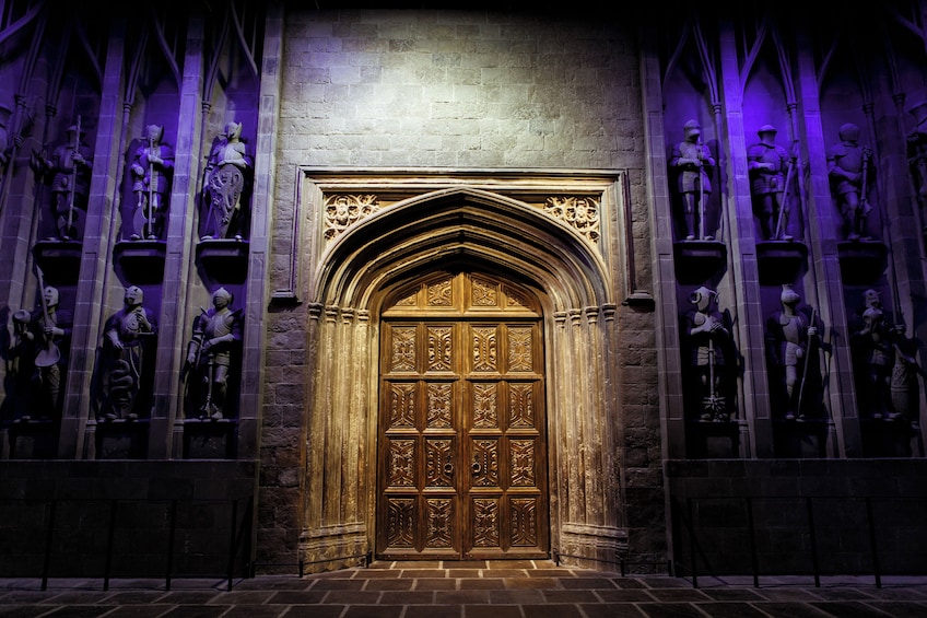 A Gothic-style door with intricate carvings, flanked by statues of knights in armor, set against a stone wall with a dark, purple-lit ambiance. 5