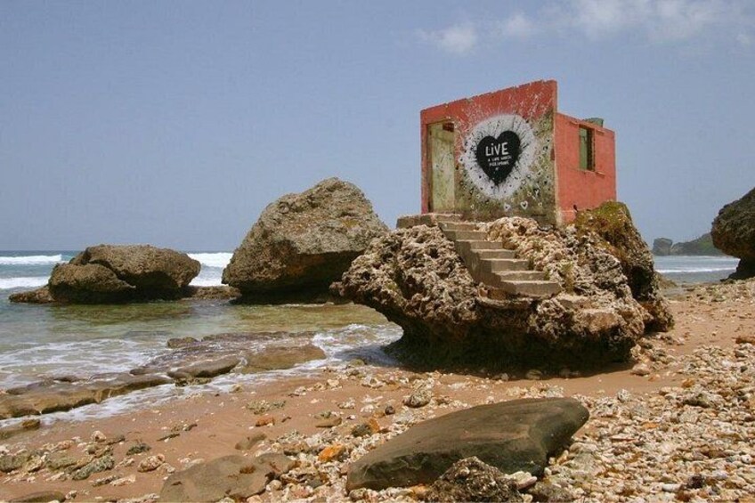 Una playa con rocas grandes, un pequeño edificio rojo con un símbolo de corazón, y una escalera que lleva hasta él. 3