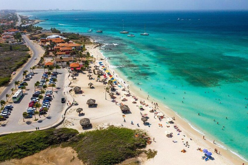 Una playa costera con aguas turquesas cristalinas, un estacionamiento y sombrillas de playa. 3