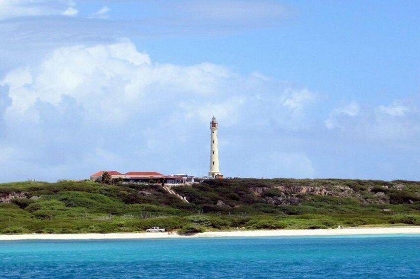 Un faro sobre una colina cubierta de hierba, con una playa en primer plano y un cielo despejado. 5