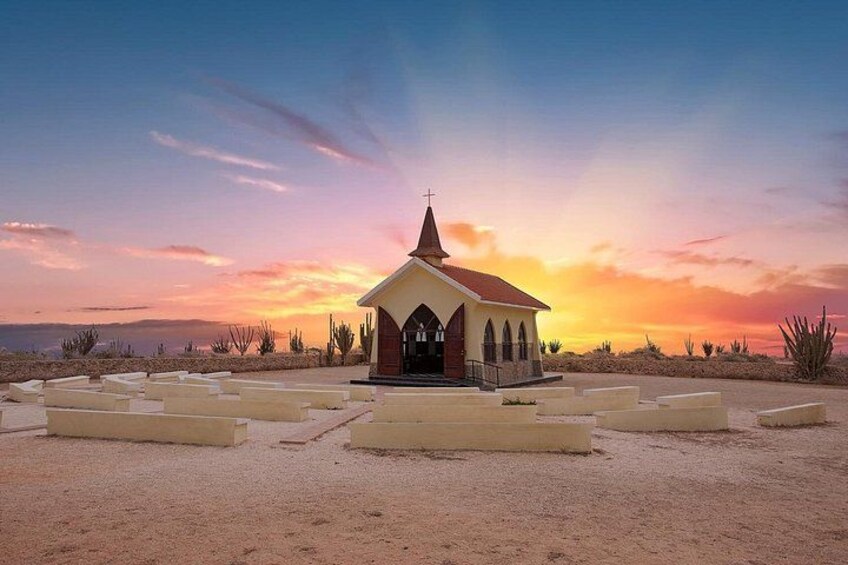 Una pequeña iglesia con una cruz en la cima, rodeada de cactus del desierto y un cielo al atardecer. 4