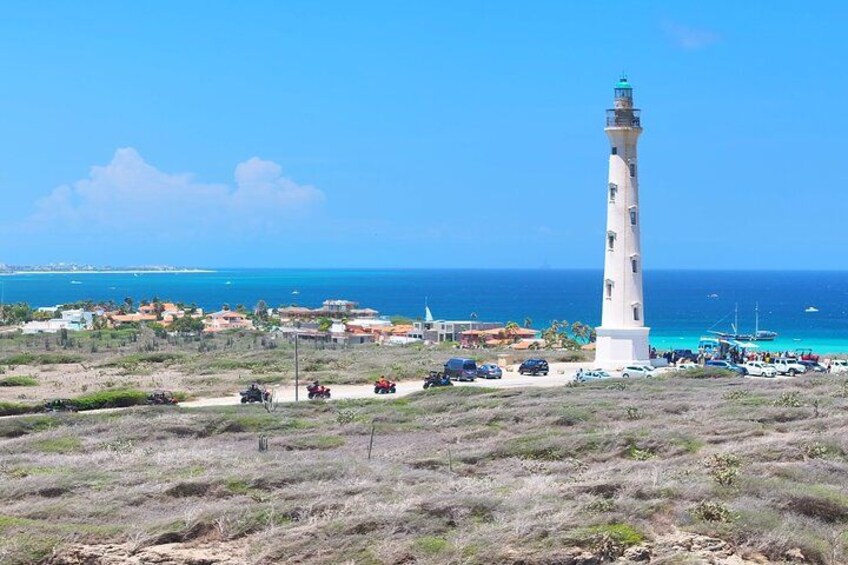 A coastal landscape with a lighthouse, vehicles, and buildings near the shore. 2