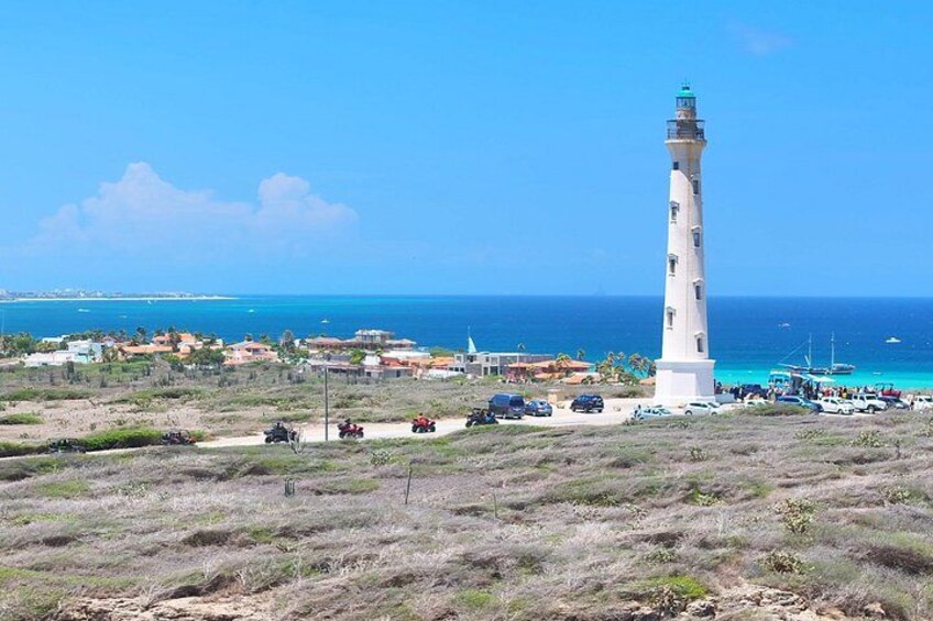 Zona costera con un faro, vehículos y edificios cerca de la playa. 2