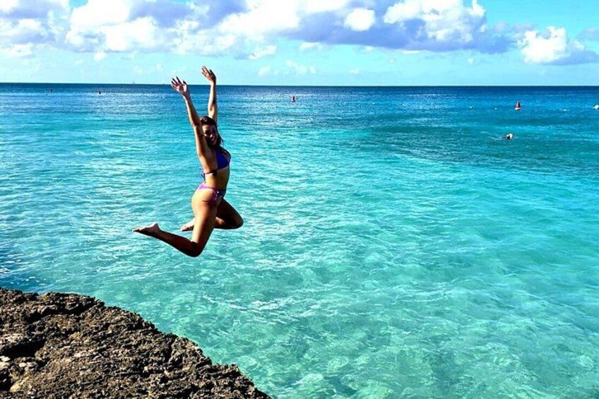 Une personne sautant d’une falaise rocheuse dans une eau turquoise et cristalline. 2