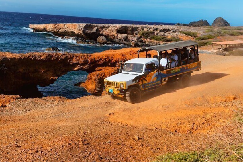 A vehicle driving on a sandy path near a rocky coastline. 1