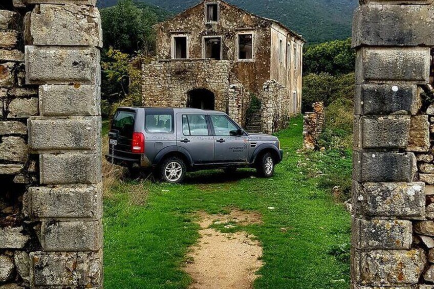 Ein grauer SUV vor einem Gebäude aus Stein, ein Feldweg führt dorthin. 5