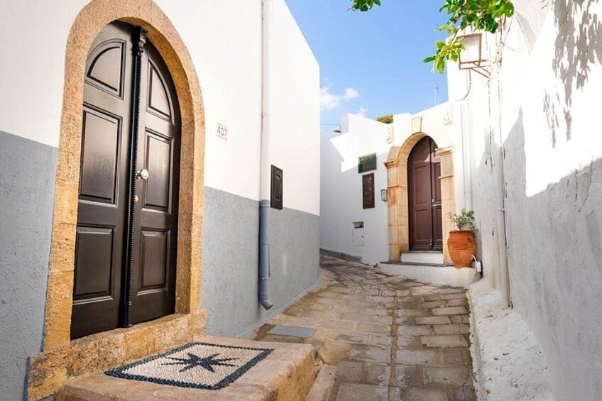 A narrow alleyway with white and blue walls, a stone pathway, and a black door with a star pattern on the mat. 2