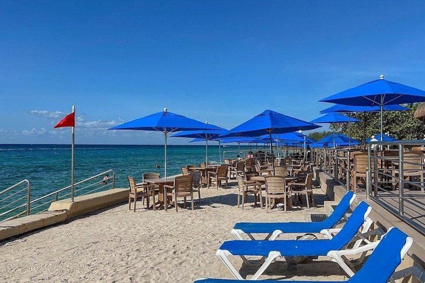 Una spiaggia con ombrelloni blu, lettini e una bandiera. 2