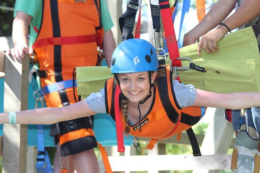 A person in a blue helmet and orange safety vest, wearing a harness, preparing for an activity. 1