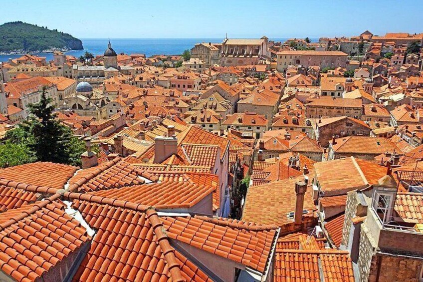 A coastal cityscape with terracotta-roofed buildings, a prominent dome, and a clear view of the sea. 2