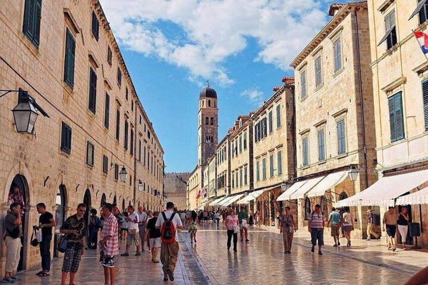 A pedestrian street lined with historic buildings, a prominent tower in the background, and people walking. 3