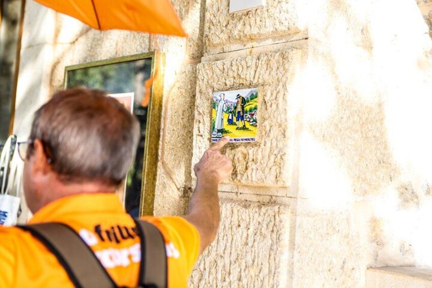 Eine Person in einem gelben Hemd zeigt auf ein Plakat an einer Steinmauer. 3