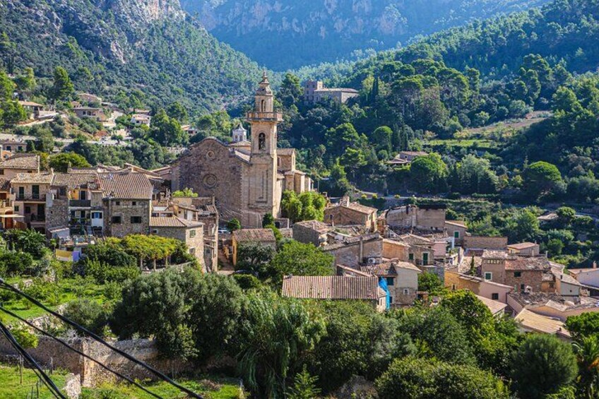 A village with a prominent church, lush greenery, and mountainous terrain in the background. 1