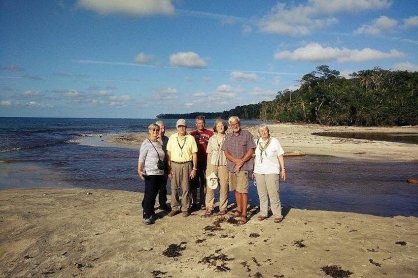 Eine Gruppe von Menschen steht an einem sandigen Strand, im Hintergrund ein ruhiges Meer und ein klarer Himmel. 4