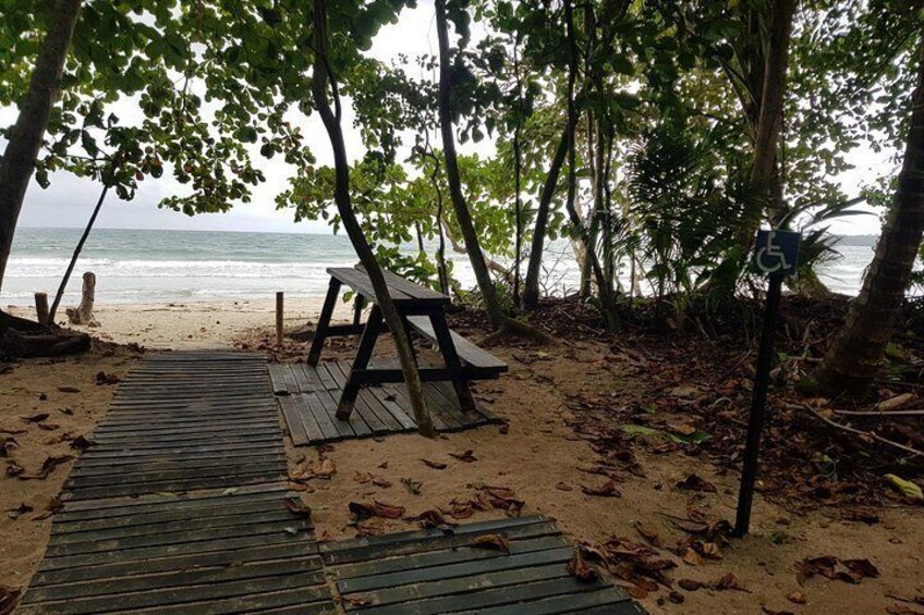 Ein Holzsteg führt zu einem Strand, wo eine Bank und ein Schild für Barrierefreiheit zu sehen sind. 5