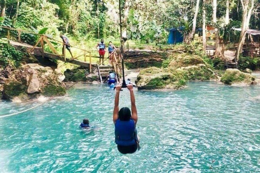 A person hanging from a rope over a body of water surrounded by greenery. 4