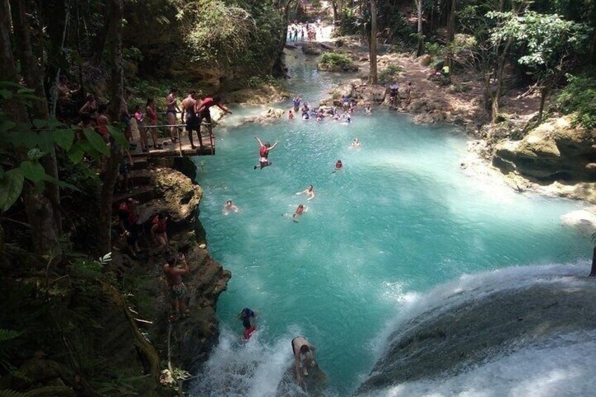 A natural hot spring with people swimming and relaxing in the water, surrounded by forested cliffs. 4
