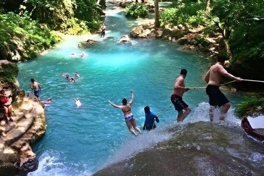 People jumping into a clear blue river surrounded by greenery. 2