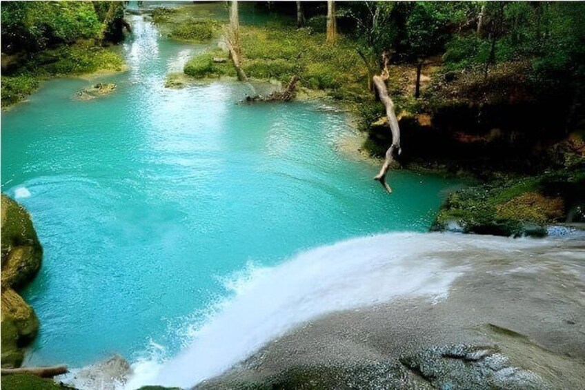 A turquoise river with a waterfall, surrounded by greenery. 3