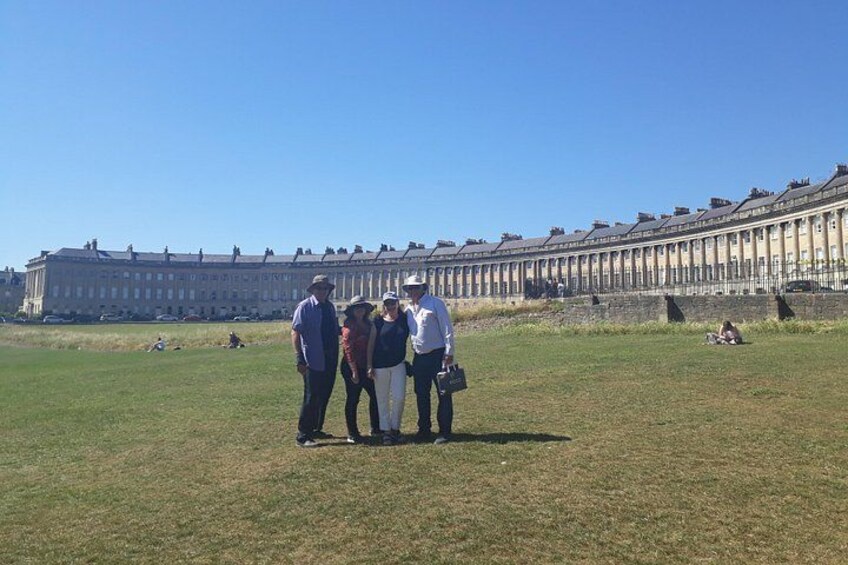 Un grupo de personas de pie en un campo cubierto de césped, con una hilera de edificios históricos al fondo. 2
