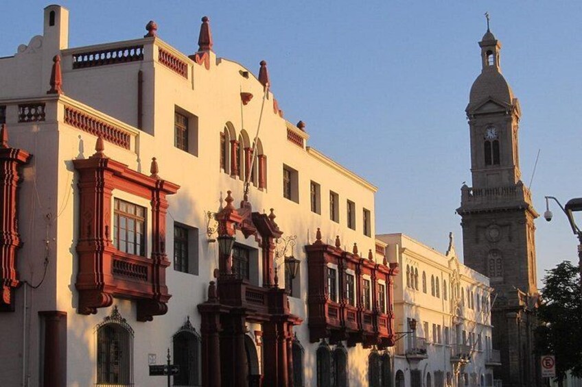 A historic street with ornate buildings, a clock tower, and a clear sky. 1