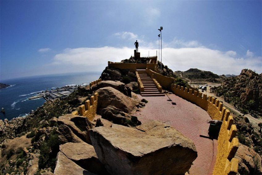 A coastal pathway with steps leading to a statue, surrounded by rocky terrain and a view of the sea. 4