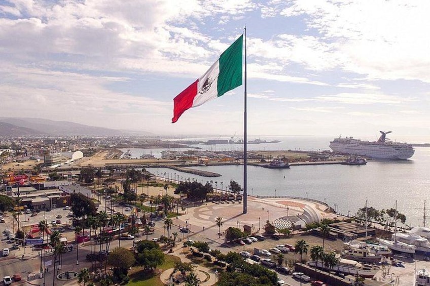 A coastal cityscape with a prominent flag, a cruise ship, and a large body of water. 2