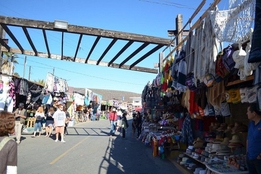 A bustling outdoor market with various stalls selling clothes and accessories. 1