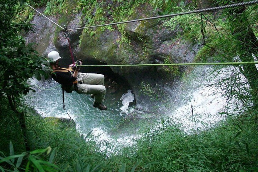 A person rappelling down a rocky cliff into a river surrounded by dense vegetation. 2